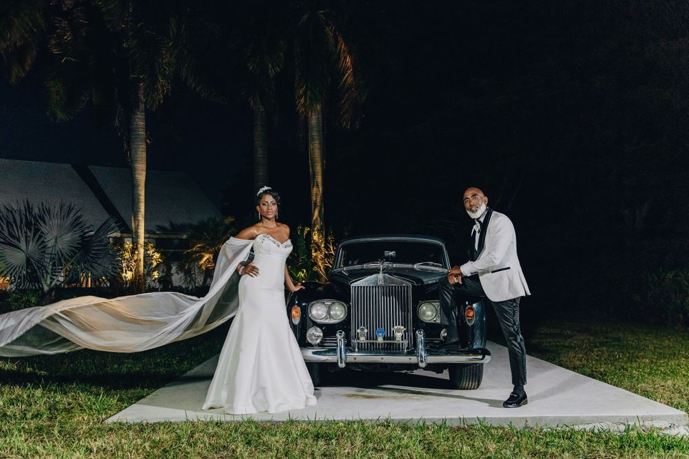 Bride with her veil beside a classic car